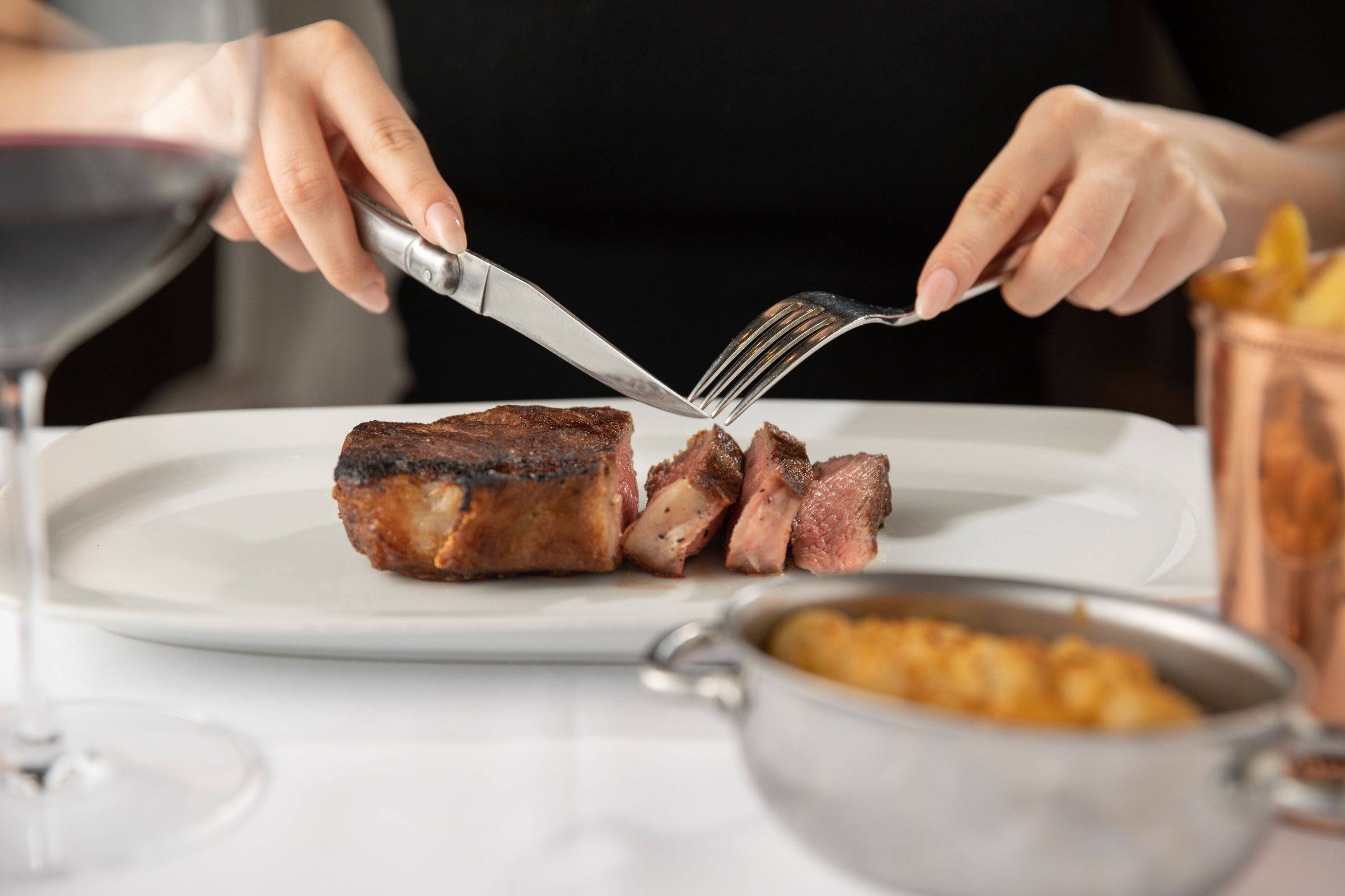 A guest slicing a USDA Prime steak at George Prime Steak, with red wine and sides