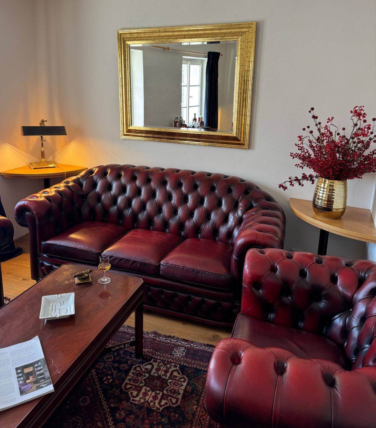 A private salon at Lví Dvůr with oxblood Chesterfields and a gilt mirror