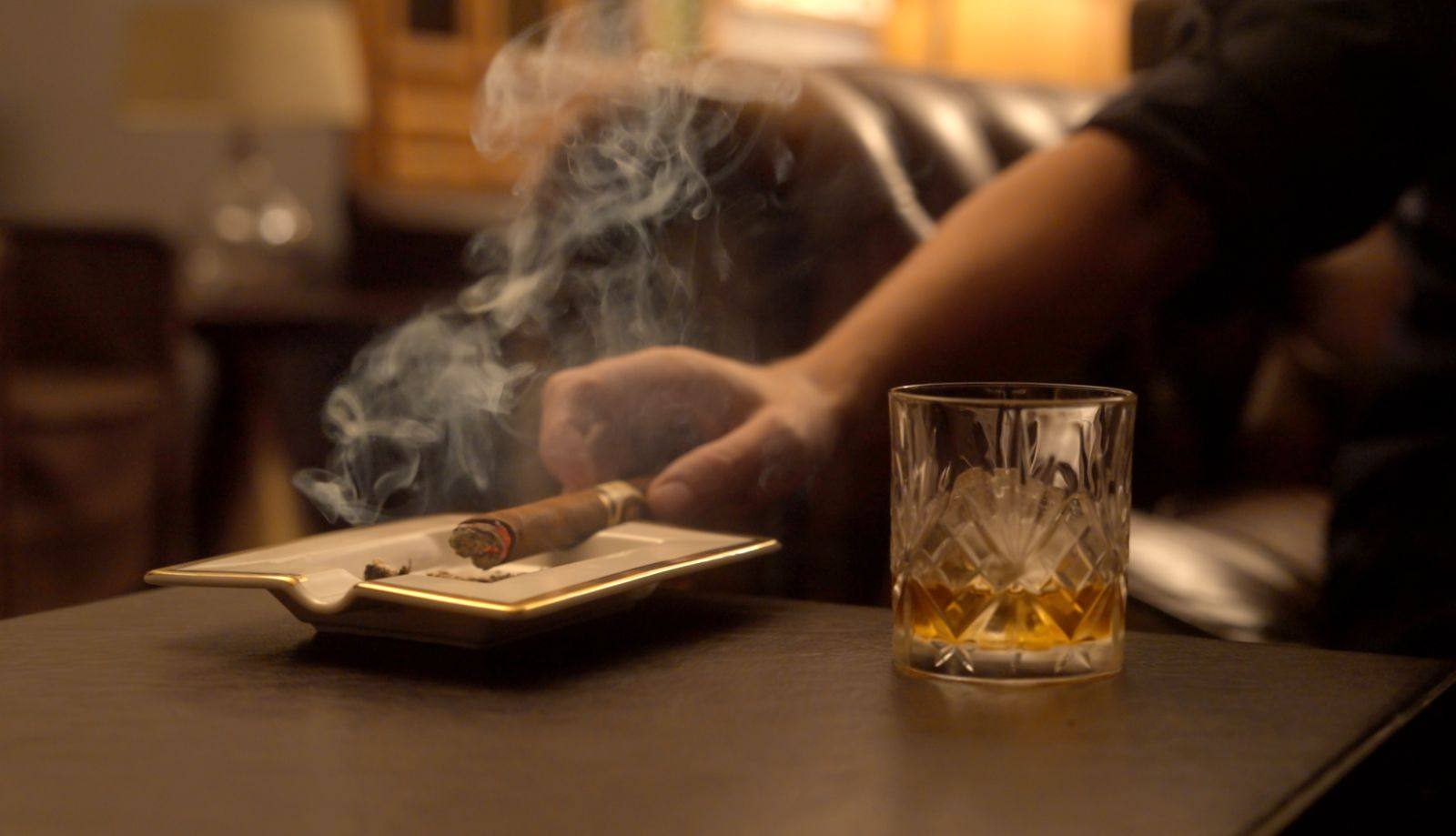 A cigar resting in an ashtray beside a glass of whisky